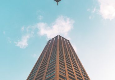 bottom view shot of airplane flying above high rise building
