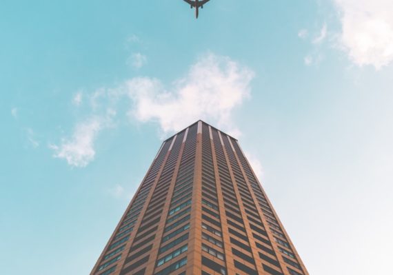 bottom view shot of airplane flying above high rise building