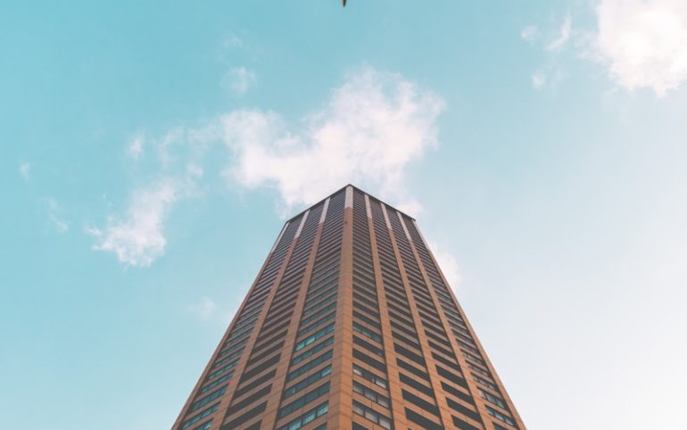 bottom view shot of airplane flying above high rise building